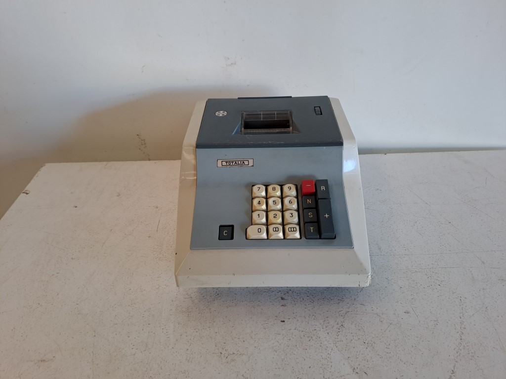 Calculadora sumadora vintage Totalia. Es un modelo de sobremesa con cuerpo de plástico bicolor (crema y gris oscuro). Lagomarsino S.p.A. fabricó estas máquinas, siendo uno de los últimos modelos mecánicos en el mercado hasta 1975. Alquiler para eventos, publicidad, series, películas