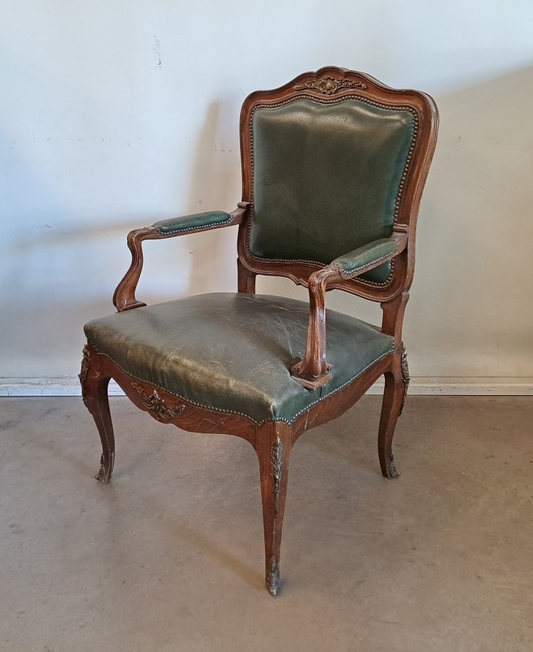 Sillón antiguo de estilo Luis XV, fabricado en madera de nogal y tapizado en cuero verde. Para alquiler de eventos, publicidad, series, películas.