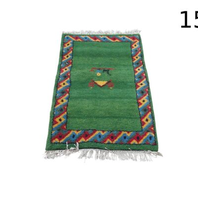 Alfombra verde pequeña estilo Gabbeh con un borde geométrico colorido y flecos blancos alquiler para eventos, publicidad, peliculas y series
