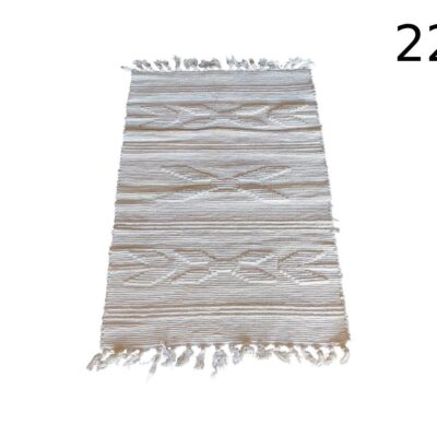 Alfombra de estilo bohemio o marroquí en tonos beige o marfil, caracterizada por su diseño geométrico lineal y flecos en los extremos alquiler para eventos, publicidad, peliculas y series