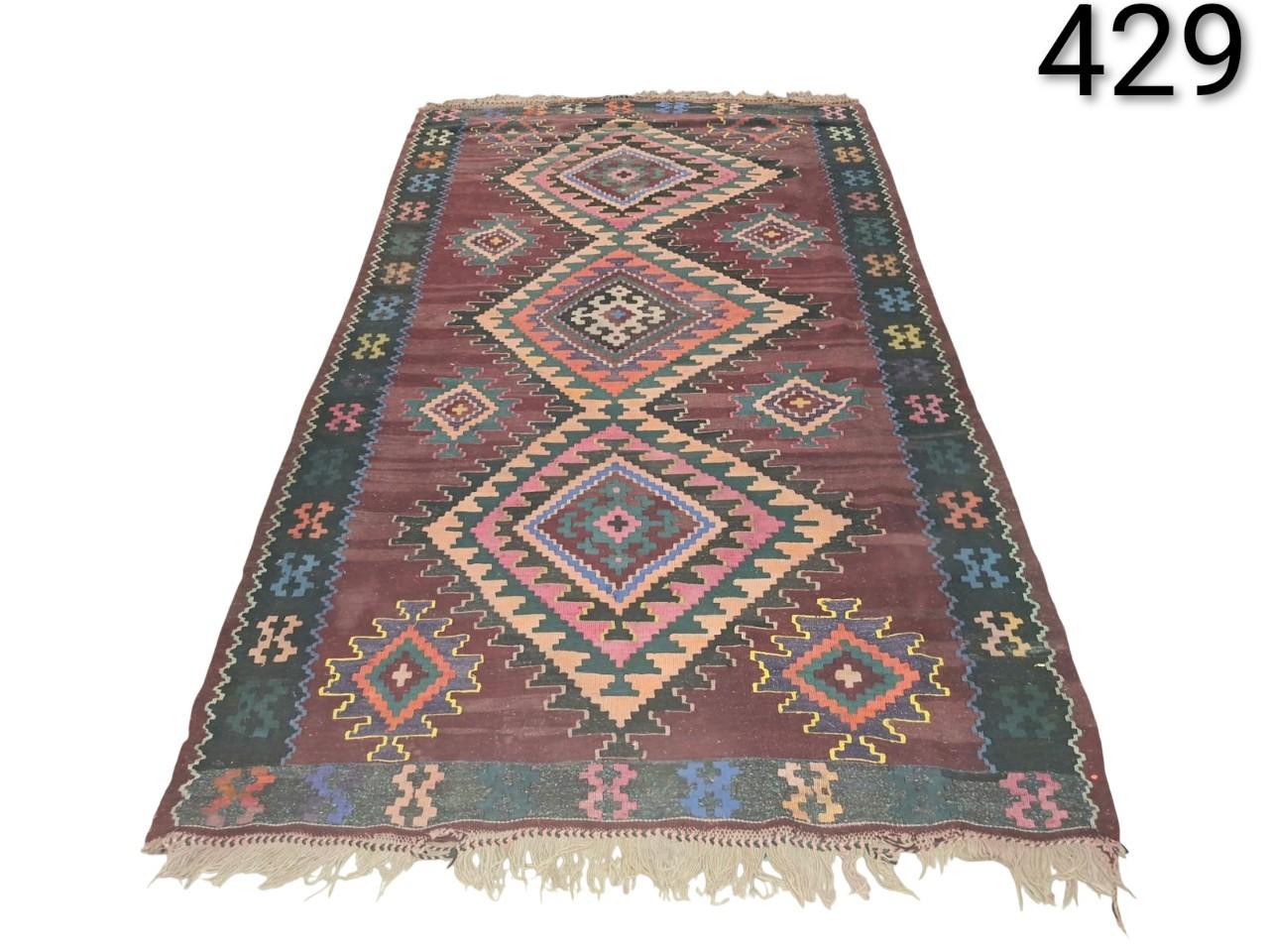 Hand-woven wool Kilim rug, with a traditional geometric design in shades of brown, pink and green, for rent for events, advertising, films and series.
