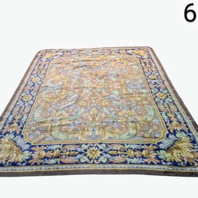 Alfombra oriental de lana, posiblemente persa o de estilo similar, caracterizada por su intrincado patrón floral y bordes decorativos en tonos azules y beige alquiler para eventos, publicidad, peliculas y series
