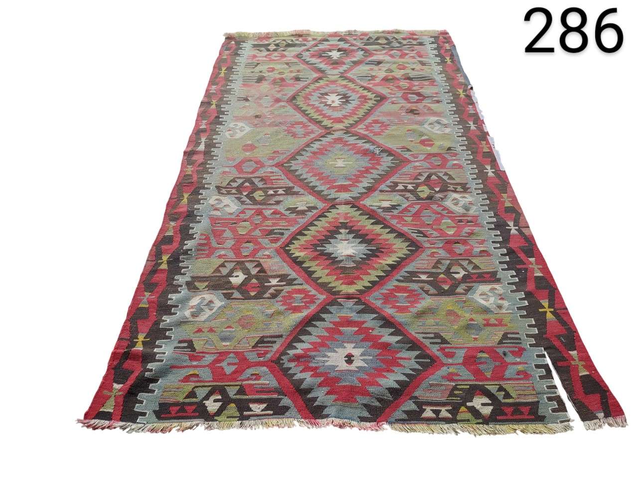 Carpet is a vintage Turkish Kilim carpet with a geometric design of diamonds in red and green tones for rent for events, advertising, films and series.