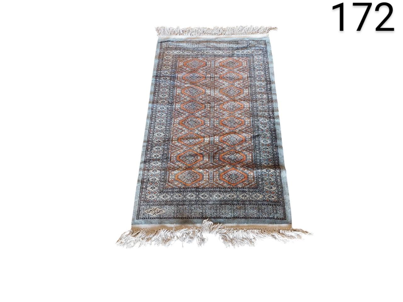 Hand knotted oriental rug with a traditional geometric design in blue and orange tones, and fringes at the ends for rent for events, advertising, films and series.
