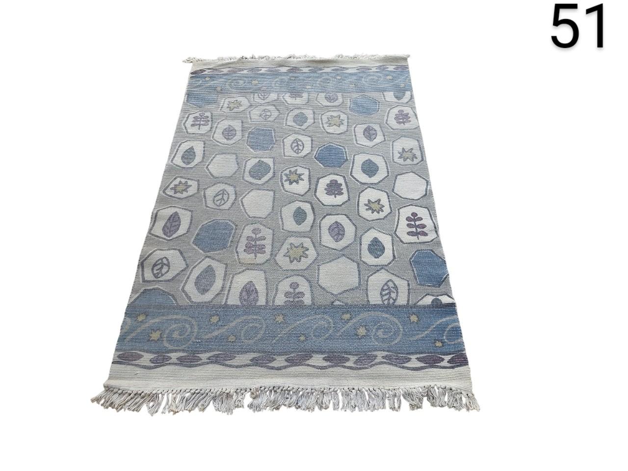 Hand-woven kilim type rug with geometric patterns in blue and grey tones, and fringes at the ends for rent for events, advertising, films and series.