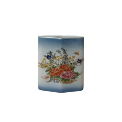 Vertical ceramic vase, characterised by a prismatic shape with a triangular cross-section and smooth edges, a white background with a blue gradient at the top and bottom, and a delicate polychrome floral arrangement painted on the front; available for hire for events, advertising, films and TV series