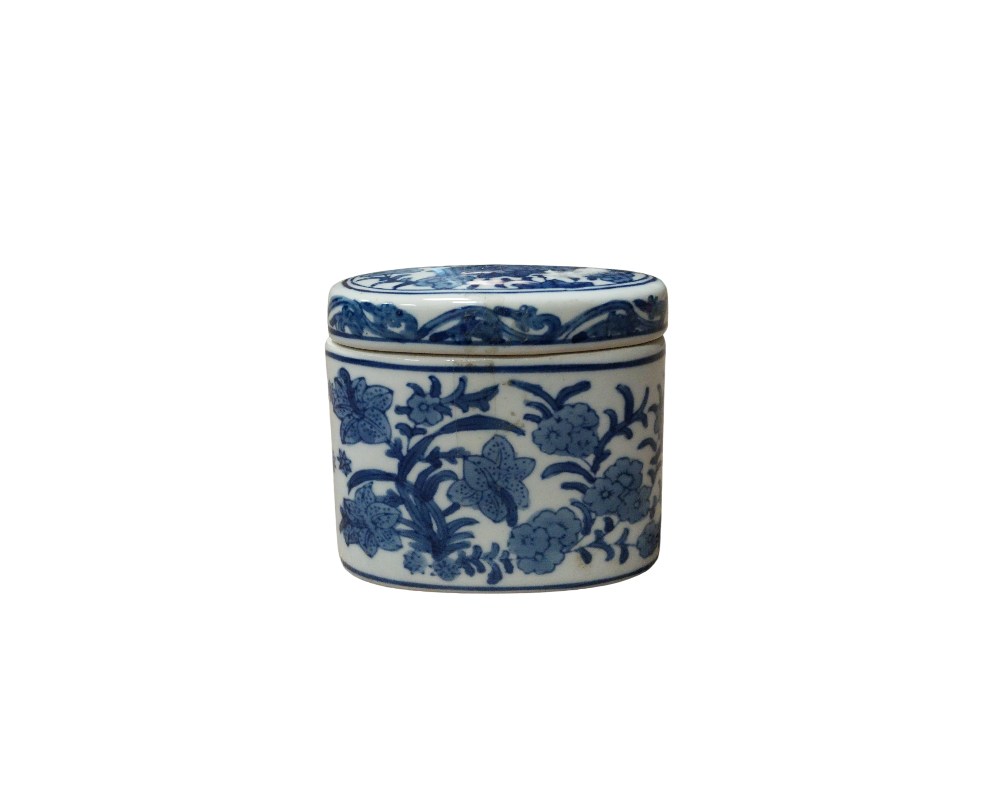 A small cylindrical porcelain box, consisting of a base and a snap-on lid. It features delicate cobalt blue decoration on a white background, using a traditional technique from Oriental ceramics, depicting motifs of flowers and foliage intertwined around the body. Available for hire for events, advertising, films and TV series.