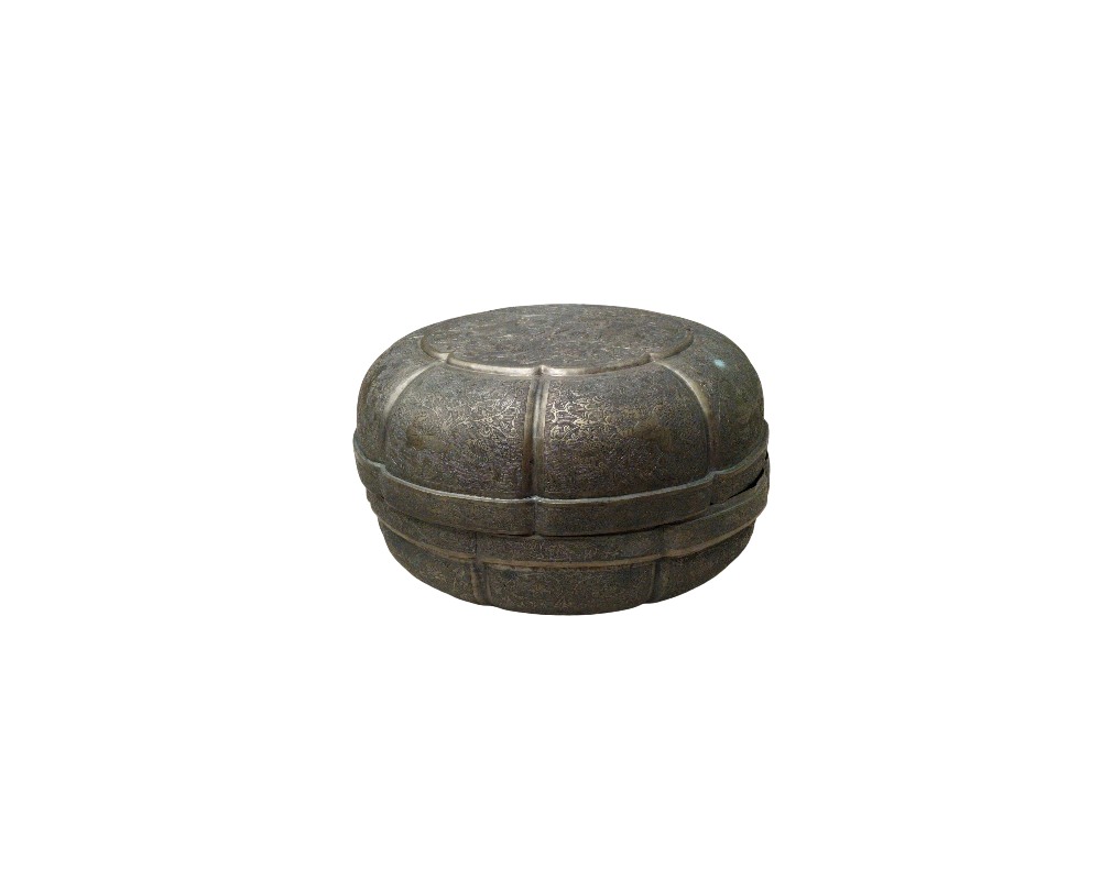A metal container with a dark, distressed finish, characterised by a circular shape with lobed sections along its outline and a surface entirely covered in finely crafted ornamental engravings; available for hire for events, advertising, films and TV series