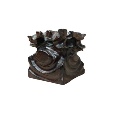 peana elaborada en madera oscura, distinguida por su tallado de formas orgánicas y fluidas que evocan elementos naturales o formaciones rocosas. A diferencia de las bases geométricas tradicionales, esta presenta un diseño más irregular y escultórico, ideal para sostener piezas decorativas que requieran un soporte con carácter propio alquiler para eventos, publicidad, peliculas y series