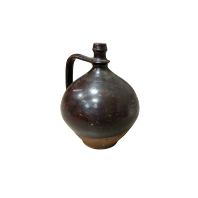 A ceramic jug with a globular body and a glossy glazed finish in dark brown tones, complemented by a visible earthen base and a side handle that connects to the narrow neck; available for hire for events, advertising, films and TV series
