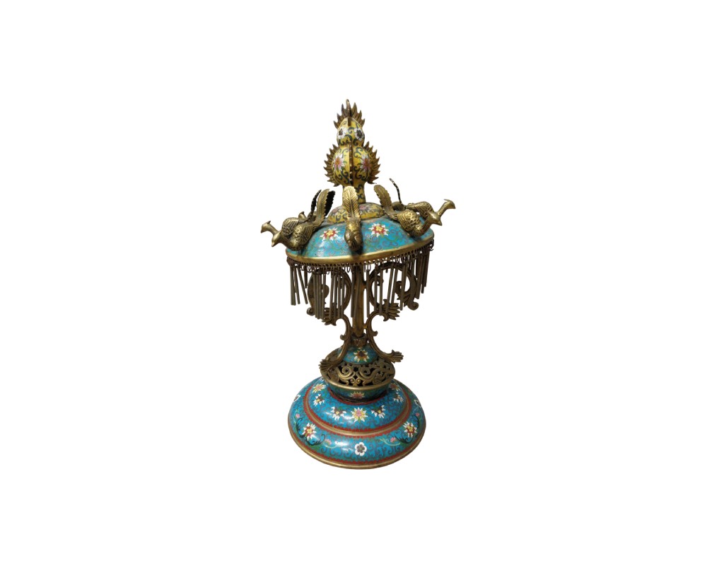 objeto decorativo de sobremesa de estilo tradicional, caracterizado por una base y una cúpula superior con esmalte cloisonné en tonos azules y motivos florales, adornada con figuras metálicas de aves en la parte superior y un faldón de colgantes metálicos alquiler para eventos, publicidad, peliculas y series