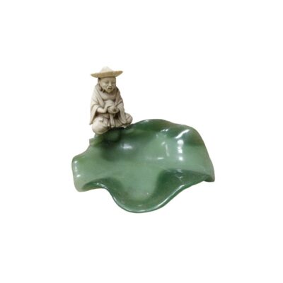 A small carved figurine depicting a figure wearing a traditional hat in a seated position, with a sculpted leaf-shaped base in green; available for hire for events, advertising, films and TV series