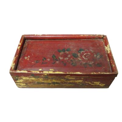 Caja de almacenamiento rectangular con tapa, elaborada en madera con un acabado tradicional de laca roja y decorada con motivos florales pintados. Presenta un aspecto desgastado que revela capas inferiores de pintura amarillenta, lo que aporta una estética rústica y antigua. Es una pieza artesanal de carácter decorativo, ideal para el resguardo de objetos pequeños o como elemento ornamental con un marcado aire tradicional.
