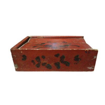 Caja de almacenamiento rectangular con tapa, elaborada en madera con un acabado tradicional de laca roja y decorada con motivos florales pintados. Presenta un aspecto desgastado que revela capas inferiores de pintura amarillenta, lo que aporta una estética rústica y antigua. Es una pieza artesanal de carácter decorativo, ideal para el resguardo de objetos pequeños o como elemento ornamental con un marcado aire tradicional.