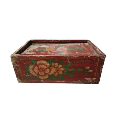 Caja de almacenamiento rectangular con tapa, elaborada en madera con un acabado tradicional de laca roja y decorada con motivos florales pintados a mano. Presenta un notable desgaste superficial que realza su carácter rústico y antiguo. Es una pieza artesanal con valor decorativo, adecuada para el resguardo de objetos pequeños o como elemento ornamental con una marcada estética tradicional.