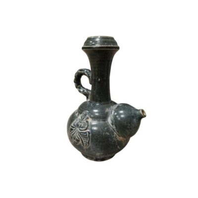A ceramic jug with a distinctive glazed finish in dark tones and a crackled effect, characterised by a globular body featuring a moulded floral relief, a curved side handle, a tall neck that widens at the top, and a side spout. Available for hire for events, advertising, films and TV series