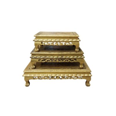 Rectangular wooden pedestals of various sizes arranged in a staircase formation, characterised by an aged gold finish, tops with moulded edges and skirting panels decorated with openwork carvings of traditional motifs, resting on curved legs; available for hire for events, advertising, films and TV series