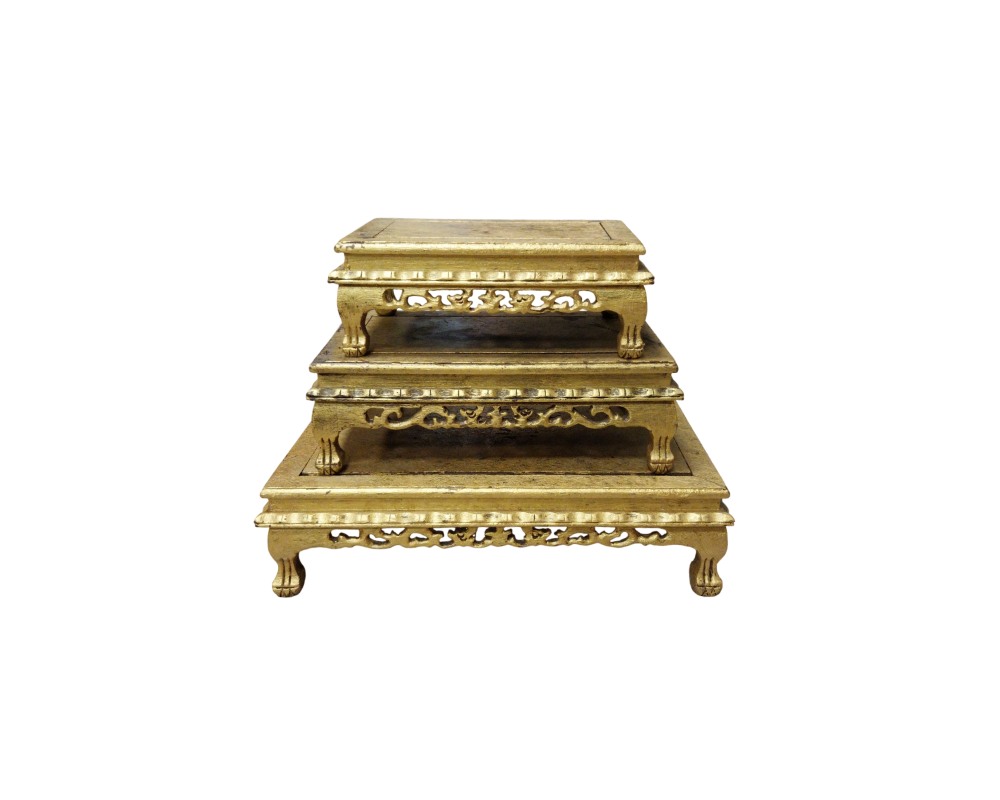 Rectangular wooden pedestals of various sizes arranged in a staircase formation, characterised by an aged gold finish, tops with moulded edges and skirting panels decorated with openwork carvings of traditional motifs, resting on curved legs; available for hire for events, advertising, films and TV series