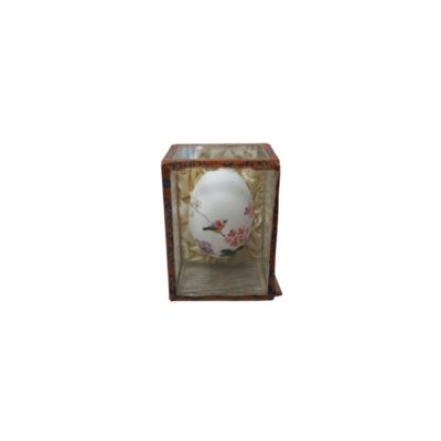 A small, egg-shaped object in shades of white, delicately hand-painted with floral motifs and a bird perched on a branch. It is displayed inside a display case or upright box with a structure covered in patterned fabric and an interior lined with soft fabric; available for hire for events, advertising, films and TV series.