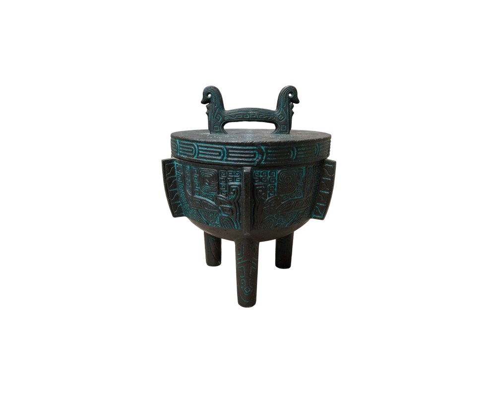 Recipiente trípode metálico con tapa, diseñado con una estética que evoca los antiguos bronces ceremoniales chinos. La pieza está decorada con intrincados relieves geométricos y patrones taotie resaltados con tonos azulados sobre una base oscura. Cuenta con un asa superior estilizada y tres patas firmes, siendo una pieza de alto valor estético, ideal como objeto de colección o elemento decorativo de gran presencia en interiores de estilo clásico.