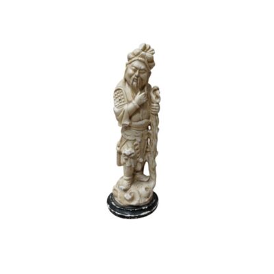 A statuette carved in an ivory-coloured tone, depicting a traditional bearded male figure wearing intricately detailed clothing and holding an ornate walking stick, resting on a dark circular base; available for hire for events, advertising, films and TV series