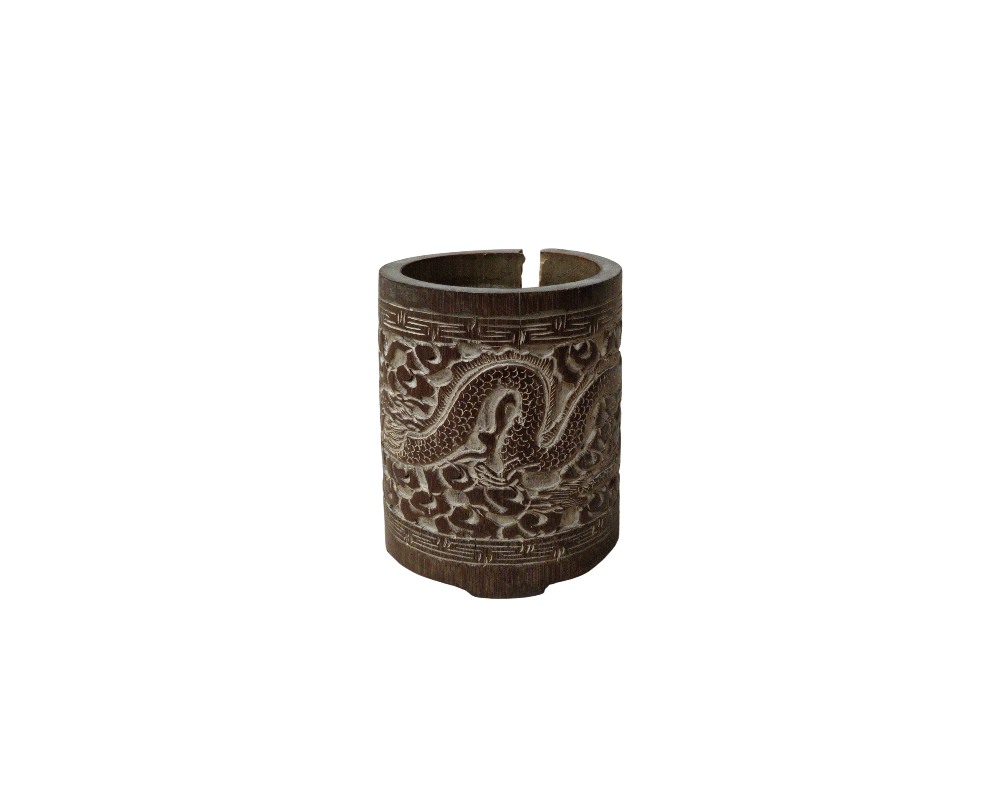 A cylindrical wooden object with a dark brown finish, featuring a carved relief on its outer surface depicting a winding dragon surrounded by cloud-like or stylised motifs, framed by geometric borders; available for hire for events, advertising, films and TV series