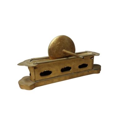 An elongated metal object with a gold finish, characterised by a decorated base, a rectangular body perforated with lobed openings on its sides, and an upper structure incorporating a vertical circular disc with an elongated stem and ornamental engravings; available for hire for events, advertising, films and TV series