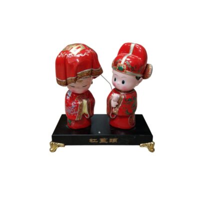 It depicts a bride and groom dressed in traditional oriental-style wedding attire, with red as the predominant colour, symbolising good fortune and celebration. The figures, designed in a delicate and stylised manner, stand on a black rectangular base with gold detailing at the corners. Available for hire for events, advertising, films and TV series.
