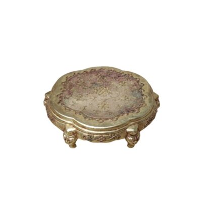 Pequeña plataforma de exhibición con acabado dorado y ornamentación detallada, caracterizada por su forma lobulada y patas esculpidas con motivos zoomorfos. La superficie superior presenta un patrón grabado de motivos vegetales y florales. Este tipo de objeto es funcional para elevar y realzar piezas decorativas, como jarrones o figuras, actuando como un pedestal ornamental sobre mesas o repisas.