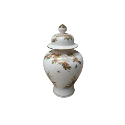 A white porcelain vase with a glossy finish, characterised by a globular shape, a stable base, a short neck and a matching lid with a gold-coloured trim. Its surface is delicately decorated with traditional motifs depicting trees, landscapes and birds in flight, with details in gold and polychrome tones. Available for hire for events, advertising, films and TV series.