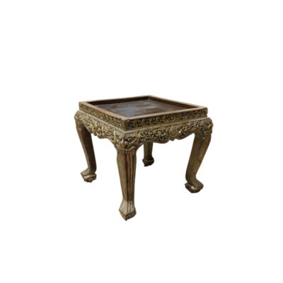 A low wooden stand, characterised by a square top with moulded edges, skirting richly decorated with fine relief carvings finished in an aged gold effect, and sturdy curved legs with ornamental details; available for hire for events, advertising, films and TV series