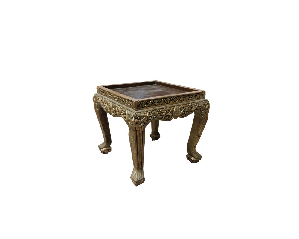A low wooden stand, characterised by a square top with moulded edges, skirting richly decorated with fine relief carvings finished in an aged gold effect, and sturdy curved legs with ornamental details; available for hire for events, advertising, films and TV series