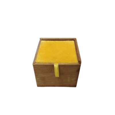 A small, square wooden box in natural tones, featuring a padded lid lined with bright yellow fabric and a small vertical ribbon in the same shade to make it easier to open; available for hire for events, advertising, films and TV series