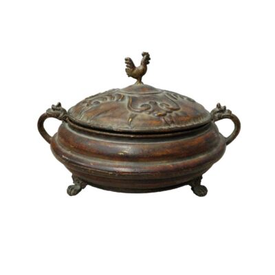 Esta elegante pieza de artesanía destaca por su cuidada ornamentación metálica y su diseño clásico. El recipiente, que incluye una tapa con un distintivo remate en forma de ave y asas laterales trabajadas, es una muestra de equilibrio y detalle decorativo. Ideal para realzar la estética de mesas o aparadores, este contenedor aporta un toque de distinción histórica y sofisticación a cualquier ambiente, siendo perfecto tanto para coleccionistas como para quienes valoran las piezas con carácter tradicional.