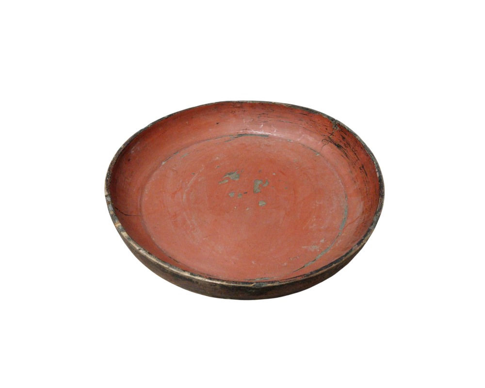 A circular wooden tray, characterised by a low-rimmed design and an interior surface with a traditional reddish finish, showing signs of use and wear consistent with its age. Available for hire for events, advertising, films and TV series.