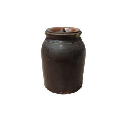 A ceramic vessel with a dark, brown-toned finish, characterised by a sturdy cylindrical shape, a body that widens slightly in the middle, a wide rimmed opening and a snug-fitting lid featuring a small central handle; available for hire for events, advertising, films and TV series