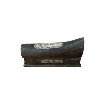 A small object with a curved profile and a rectangular base, made from a dark material with an antique appearance, featuring decorative inlays with calligraphic inscriptions. Its small size confirms its function as a wrist rest, a desk accessory traditionally used by calligraphers to raise the hand and prevent smudging the paper whilst writing. It is a refined collector’s item that combines technical utility with a distinct historical aesthetic.