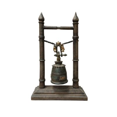 A decorative object comprising a traditional-style metal bell, suspended by a cord between two vertical posts with rectangular bases. The bell features engraved details with gold finishes that contrast with its dark, weathered surface. It is a handcrafted piece with a distinctly classical and ritualistic aesthetic, ideal as a table centrepiece for spaces seeking a touch of historical and cultural elegance.