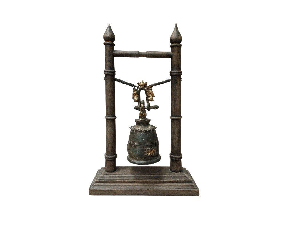 A decorative object comprising a traditional-style metal bell, suspended by a cord between two vertical posts with rectangular bases. The bell features engraved details with gold finishes that contrast with its dark, weathered surface. It is a handcrafted piece with a distinctly classical and ritualistic aesthetic, ideal as a table centrepiece for spaces seeking a touch of historical and cultural elegance.