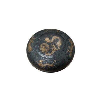 A circular box with a dark-coloured finish, featuring an intricate embossed design on the top surface with gold detailing depicting a central dragon surrounded by complementary motifs; available for hire for events, advertising, films and TV series