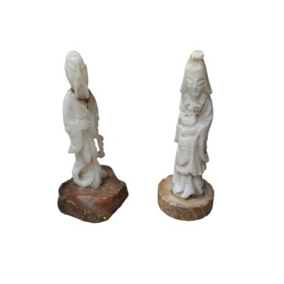 This pair of statuettes depicts human figures dressed in traditional clothing, carved from light-coloured stone – possibly jade or a similar material – and standing on bases made of natural stone in darker, earthy tones. Available for hire for events, advertising, films and TV series.