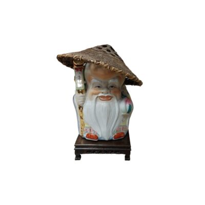 A glazed ceramic figurine depicting a wise old man or a smiling traditional deity, with a long white beard, a conical hat made of plaited straw and holding a walking stick, all mounted on a small carved wooden base. Available for hire for events, advertising, films and TV series.