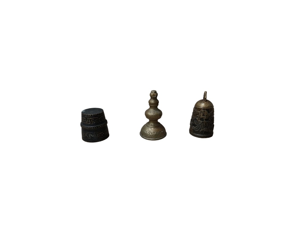 The set comprises three small metal objects in dark, weathered tones, including a thimble or cylindrical object with engraved bands, and a stupa-shaped piece or stepped finial – available for hire for events, advertising, films and TV series