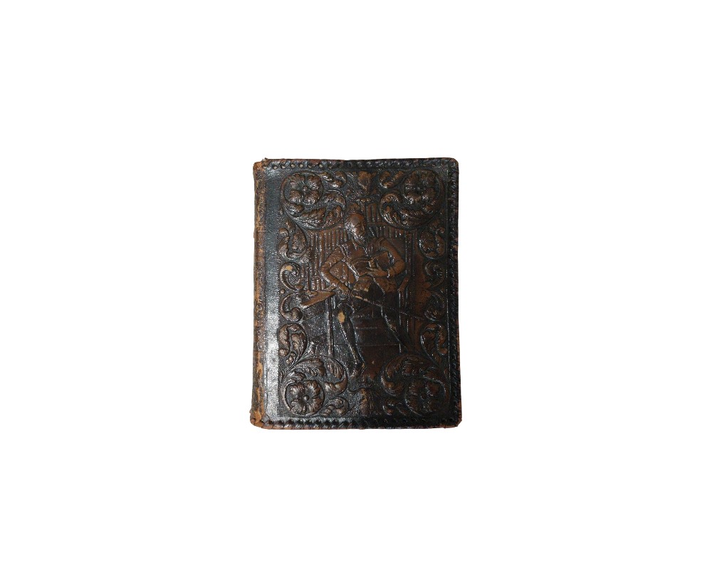 An antique hardback notebook with a dark leather cover, featuring intricate hand-embossed floral motifs and a central figure of a seated person set against a detailed background; available for hire for events, advertising, films and TV series