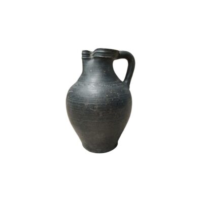 A rustic ceramic jug with a dark-toned finish and aged textures, characterised by a rounded, bulbous body, a curved side handle and a spout integrated into the upper rim. Available for hire for events, advertising, films and TV series.