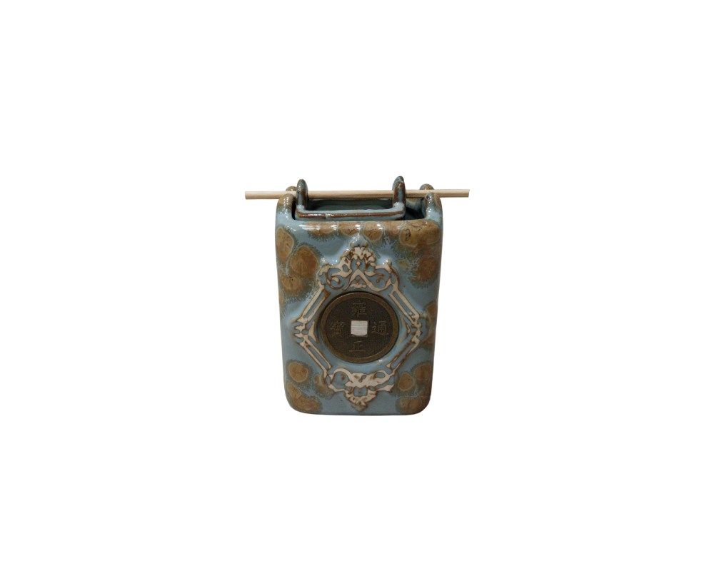 contenedor de cerámica con un acabado esmaltado en tonos azulados y marrones. Destaca por tener incrustada en su cara frontal una réplica de una moneda china antigua, rodeada por un relieve ornamental alquiler para eventos, publicidad, peliculas y series