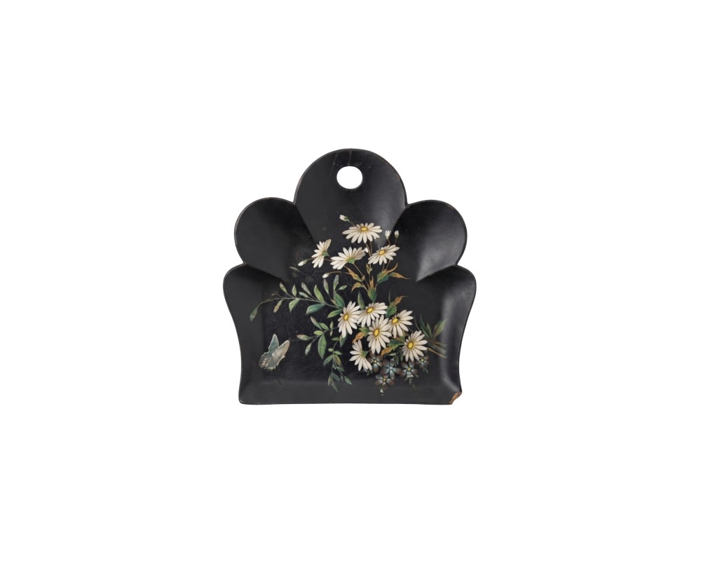 bandeja decorativa de superficie oscura y contorno lobulado, caracterizada por un orificio superior para colgar y una delicada pintura policromada en el centro que representa un ramo de margaritas blancas con hojas verdes y una pequeña mariposa alquiler para eventos, publicidad, peliculas y series
