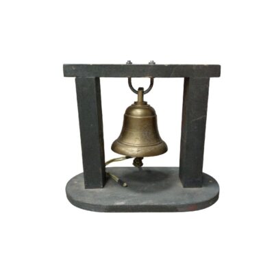 Campana metálica (posiblemente de latón o bronce) suspendida de un soporte de madera de diseño sencillo. Cuenta con un badajo funcional para emitir sonido y un cordel de accionamiento. Es una pieza de escritorio o estantería que combina una estética de inspiración marina con una función decorativa o de señalización sonora. alquiler para eventos, publicidad, peliculas y series