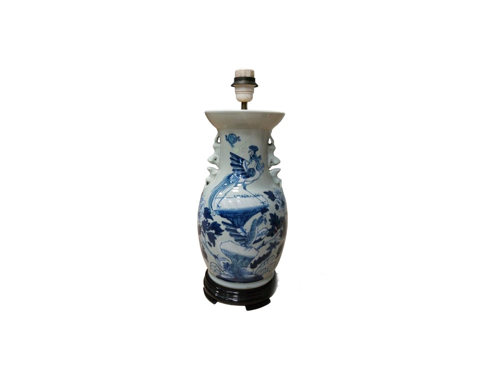 Lámpara de mesa elaborada sobre un jarrón de porcelana con decoración azul sobre fondo blanco, que presenta motivos de aves y elementos naturales. El conjunto incluye un portalámparas superior y descansa sobre una base de madera torneada alquiler para eventos ,publicidad, peliculas y series