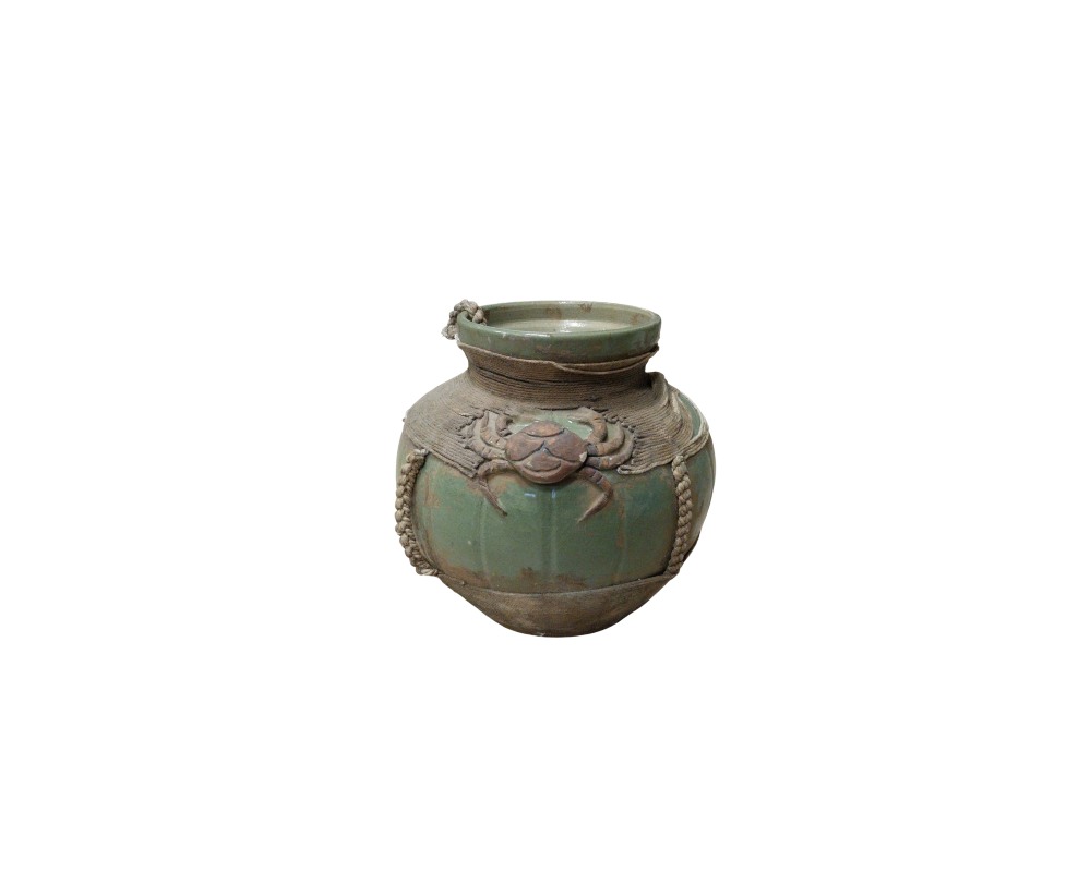 A ceramic vase with a green-toned glaze, characterised by a globular body and a distinctive design featuring a relief sculpture of a crab on the front, surrounded by elements resembling nets; available for hire for events, advertising, films and TV series